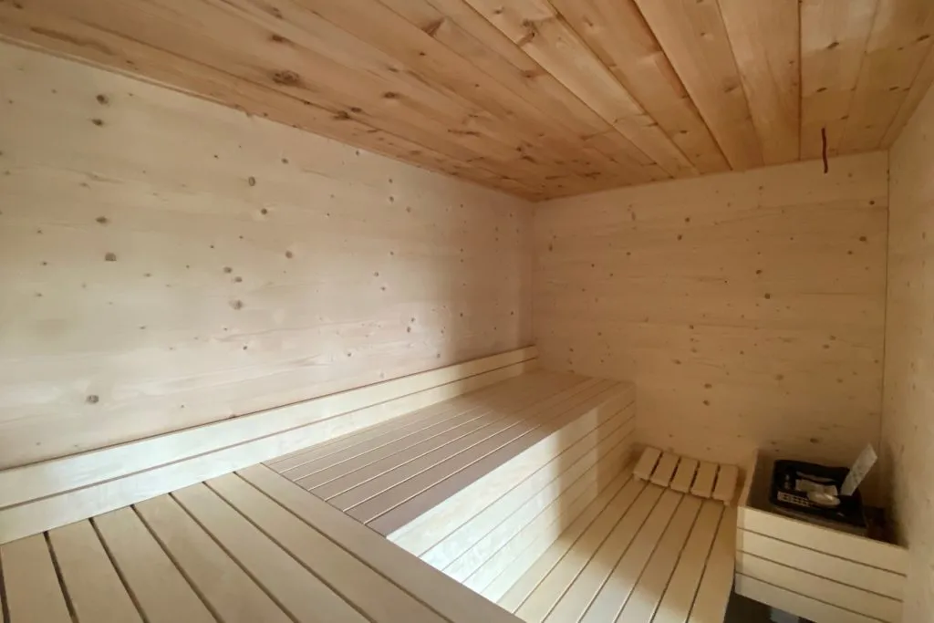 Saunakabine mit hellem Holzausbau, gestaffelten Sitzbänken und Ofen im privaten Wellnessbereich